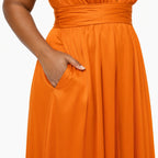 color:Orange | Close-up of a person wearing a bright orange midi dress with a gathered waistband and a side pocket, with the hand inserted into the pocket, against a plain white background.